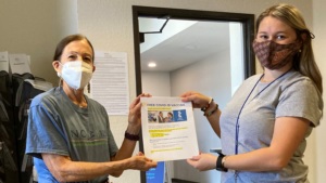 two women wearing face masks holding a vaccination resource flyer